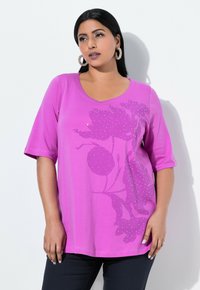 Fuchsia V-hals top med korte ærmer, blomsterdesign med rhinesten detaljer og en løstsiddende pasform, parret med mørke bukser.
