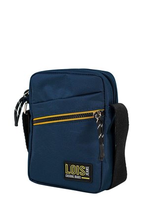 Bolsa rectangular azul marino de textil con una cremallera amarilla, una placa con el logo y una correa ajustable. Presenta una superficie texturizada.