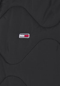 Chaqueta negra acolchada con textura con acolchado, costuras contrastantes en blanco y un pequeño logotipo bordado en rojo, blanco y azul.