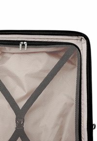 Interno di una valigia beige aperta con cinghie incrociate elastiche nere e un compartimento con zip in rete nera su un lato.