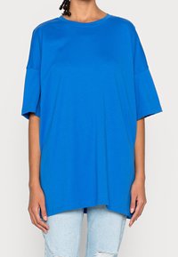 Modré oversized tričko z měkké bavlny, s kulatým výstřihem, krátkými rukávy a rovnými lemy, nošené s světlými džíny.