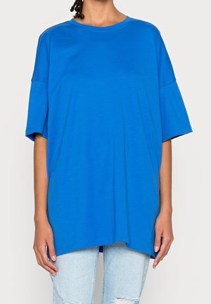 T-shirt blu oversized in cotone morbido, con collo a giro, maniche corte e orlo dritto, indossato con jeans di denim chiaro.