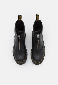 Black leather ankle boots featuring a front zipper, yellow stitching, and a chunky sole. Pull tab at the back for easy wear.