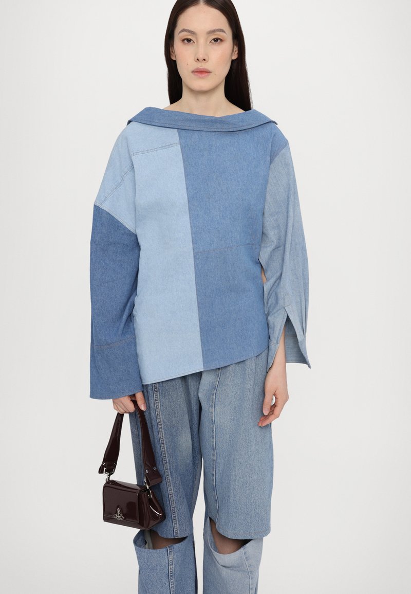 Denim top with oversized collar in light to medium blue shades, featuring wide sleeves. Paired with light blue jeans and a small burgundy handbag.