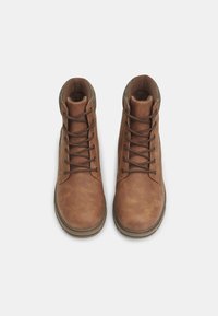 Botas de cuero marrón con superficie texturizada, puntera redonda y diseño con cordones. Presenta un cuello con acentos verdes y una suela de goma duradera.