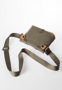 Borsa a tracolla verde oliva con un accento in pelle marrone, caratterizzata da una superficie liscia e da una tracolla in tessuto regolabile. Dettaglio con chiusura a scatto visibile.