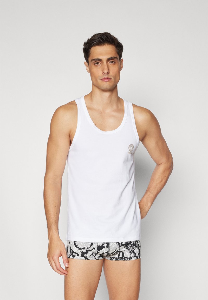 Camiseta de algodón blanca sin mangas con tirantes anchos. Presenta un pequeño logo en el pecho. Combinada con pantalones cortos negros de patrón.