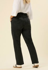 Höga svarta denimjeans med rak benform, med bakfickor och en lätt textur. Matchas med en vit skjorta och avslappnade skor.