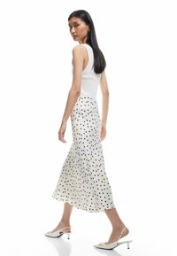 Vit linne med hög krage, kombinerat med en knälång, krämfärgad kjol med svarta prickar, och vita slingback-hälar.