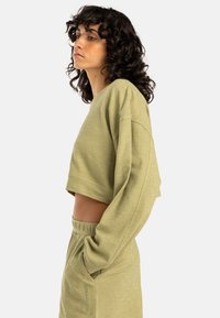 Felpa corta verde oliva con maniche larghe e una texture morbida, abbinata a bermuda a vita alta dello stesso colore con tasche laterali.