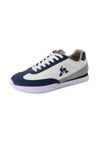 Zapatillas de deporte en azul marino y blanco con material de cuero sintético, suela de goma texturizada, detalles en gris, punta redondeada y cordones blancos.