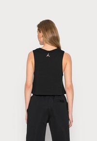 Musta lyhyt toppi, joka on valmistettu puuvillasta ja jossa on hihaton muotoilu. Takana pieni punainen Jordan-logo. Sileä pinta, minimalistinen tyyli.