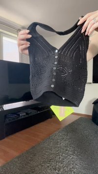 Mustahiit musta, ilma varrukat crop top nupudega ees kahte kätte hoida elutoa taustal.