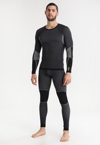 Conjunto de ropa térmica activa negra que incluye una camiseta de mangas largas y leggings. Tejido texturizado con acentos en gris contrastantes y elementos de diseño sin costuras.