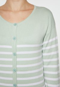 Hellgrüner Cardigan mit weißen horizontalen Streifen. Verfügt über einen runden Halsauschnitt, lange Ärmel und fünf türkisfarbene Knöpfe auf der Vorderseite.
