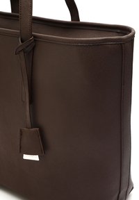 Pruun nahast käekott tekstuurse viimistlusega, lame disain, kaks sangast ja küljes kaubamärgi nimega 