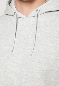Sudadera gris con una textura suave, cuerdas ajustables con ojales de metal y un corte casual.