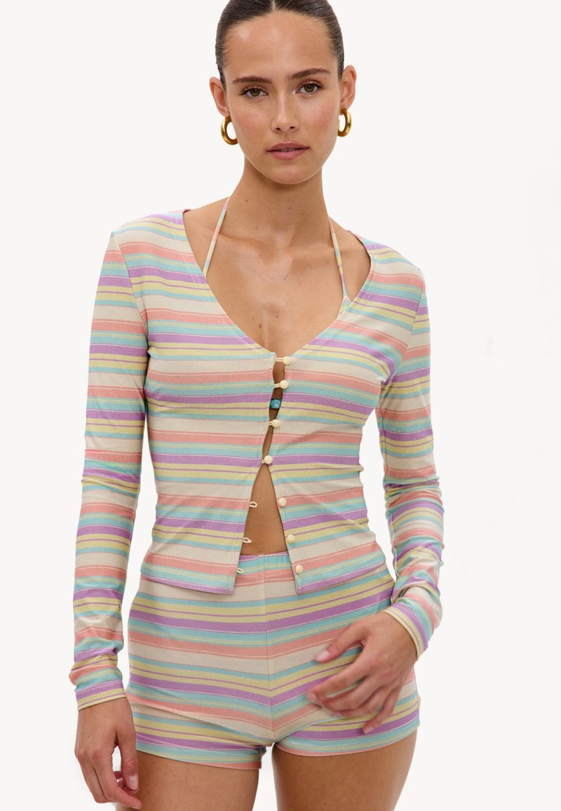 Femme portant un haut à manches longues rayé pastel avec des boutons et un short taille haute assorti, des boucles d'oreilles anneaux dorés et un haut de bikini en dessous.