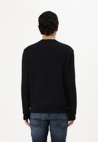 Sort sweatshirt med lange ærmer, rund hals og ribbet kant, parret med blå denim jeans med buede baglommer.