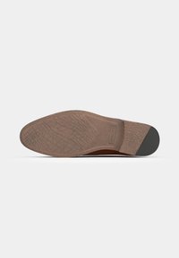 Semelle en caoutchouc marron avec un motif de grip texturé et des accents lisses. Présente une forme effilée et un léger talon.