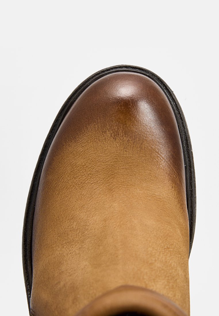 Stivaletto in pelle marrone con punta rotonda, caratterizzato da una superficie liscia e una suola in gomma nera per una maggiore resistenza.
