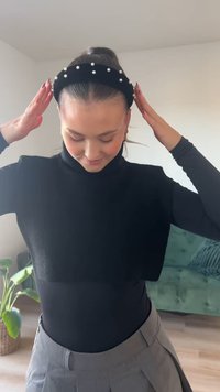 Fascia in velluto nero con perle bianche lungo la parte superiore, indossata da una persona in un dolcevita nero e una gonna grigia, in piedi all'interno.