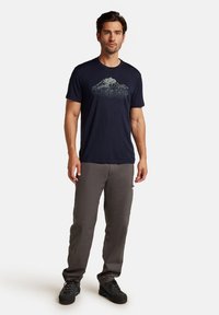 Navy blue short-sleeve t-shirt with a mountain graphic; paired with gray pants and black footwear; modern casual fit.