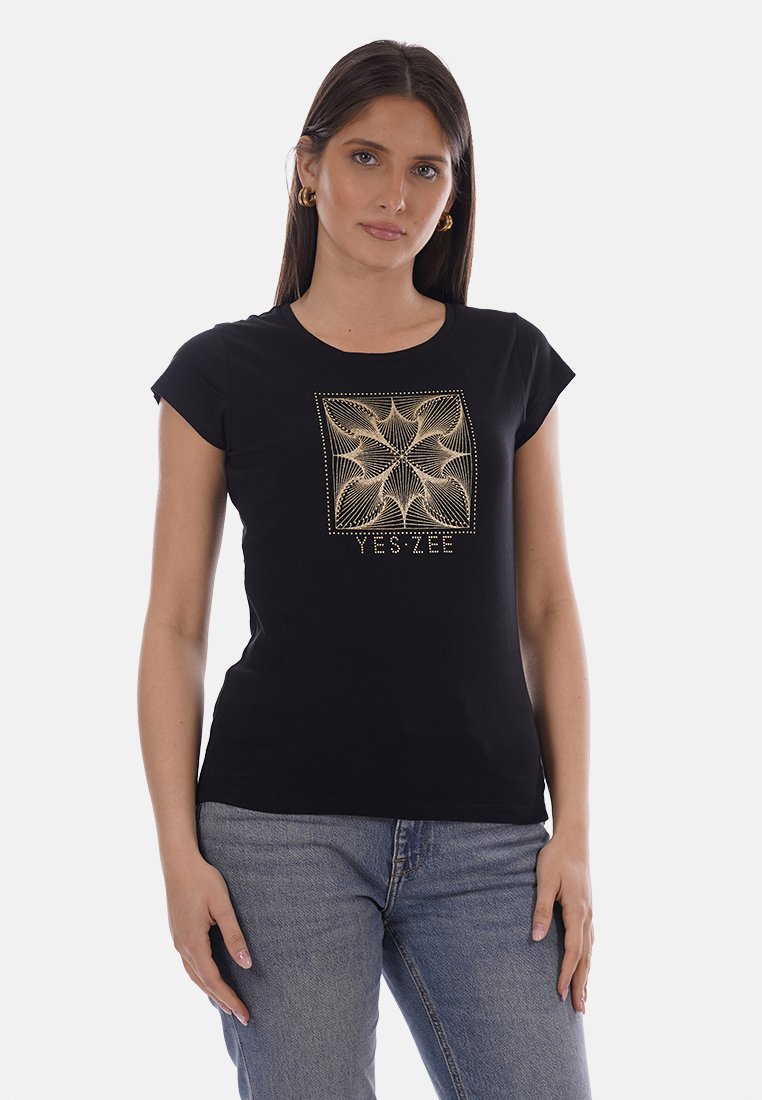 Donna che indossa una T-shirt nera aderente con un motivo geometrico dorato e la scritta "YES ZEE", abbinata a jeans di denim blu.