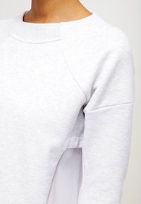 Ljusgrå sweatshirt med texturerad yta, som har raglanärmar och meshdetaljer på sidan för bättre andningsförmåga. Minimal branding.