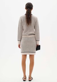 Knit two-piece set in beige with navy accents. Features a slim-fit top with long sleeves and a knee-length skirt. Smooth texture, ribbed hems.