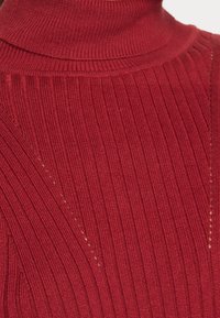 Pull à col roulé rouge côtelé avec des motifs de texture verticale et diagonale, doté d'un col ajusté et d'un tissu en maille doux.
