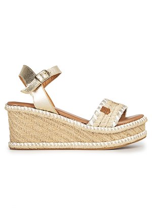 Kilesandal med flettet stråplatform, guld ankelrem med spænde og åben tå-frontrem med dekorative syninger.