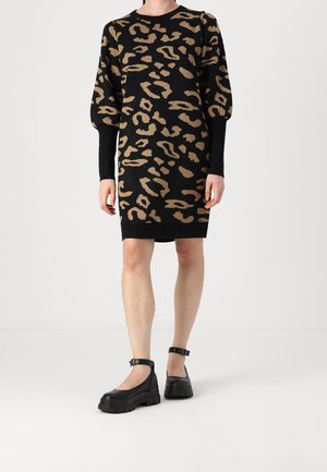 Vrouw draagt een zwart-bruine langharige trui-jurk met luipaardprint, pofmouwen en zwarte platform enkellaarsjes met bandje.