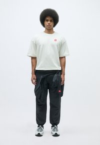 Lys grå oversized t-shirt med et lille rødt logo, parret med sorte bukser med snøring og lommer. Sorte og hvide sneakers.