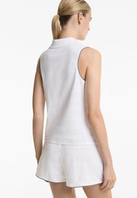 Polo sans manches blanc avec un motif à rayures texturé et des bordures de couleur marine contrastantes au niveau des emmanchures, associé à un short blanc.