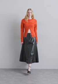 Pulover tricotat pufos de culoare portocalie, cu o decupare frontală, asociat cu o fustă lungă din piele neagră, dotată cu fermoare laterale. Cizme cu toc stilou finalizează look-ul.