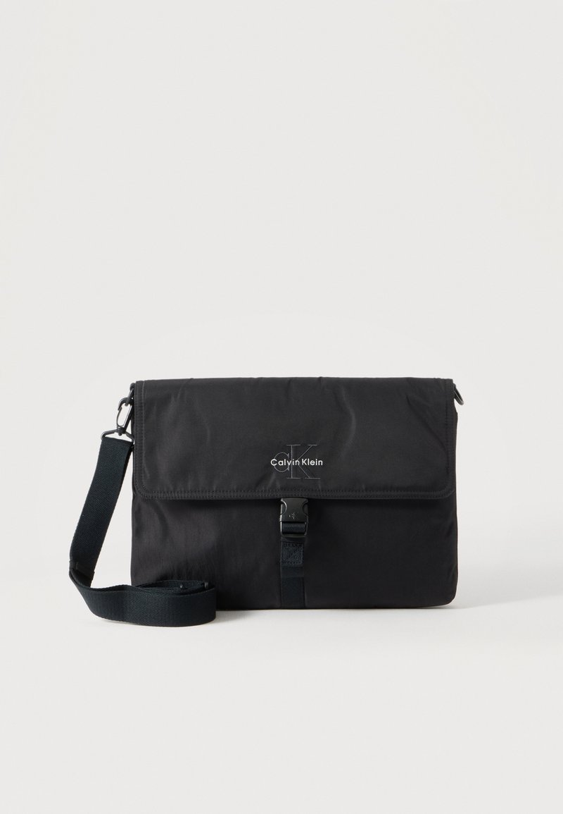Sac messager noir Calvin Klein avec bandoulière réglable et rabat avant sécurisé par une boucle, présenté sur un fond uni.