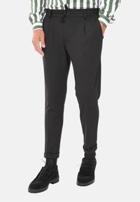 Czarne zwężane spodnie z elastycznym pasem, bocznymi kieszeniami i gładką fakturą, w połączeniu z czarnymi zamszowymi butami.