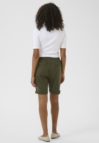 Shorts verts olive à coupe décontractée, ourlets retroussés et ceinture élastique. Associés à une chemise blanche ajustée à manches courtes.