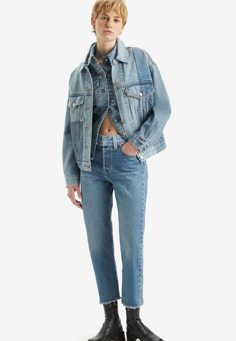 Lichtblauwe spijkerjacket met twee voorzakken en vervaagde textuur, gecombineerd met bijpassende high-waisted jeans en zwarte enkellaarsjes.