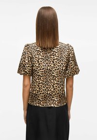 Bluza s leopard uzorkom od satenske tkanine ima kratke napuhane rukave i okrugli izrez, u kombinaciji s crnom suknjom.