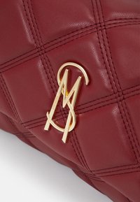 Sac à main en cuir matelassé bordeaux avec accent logo doré. Présente un motif en diamant surpiqué et une texture douce.