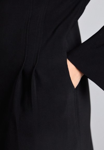 Black garment featuring a side pocket, constructed of smooth fabric with subtle seam detailing, creating an elegant, tailored appearance.