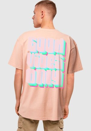 T-shirt di cotone rosa chiaro con una grande grafica sul retro in testo audace e multicolore: "BUONE VIBRAZIONI SOLO" con effetti 3D.