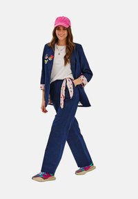 Džínová blazer a kalhoty s růžovými puntíky. Bílá košile, růžová kšiltovka a barevné tenisky doplňují outfit.