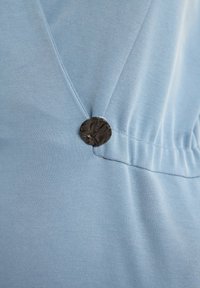 Jasnoniebieska tkanina o gładkiej fakturze, z ciemnym, teksturowanym guzikiem akcentującym marszczenie.