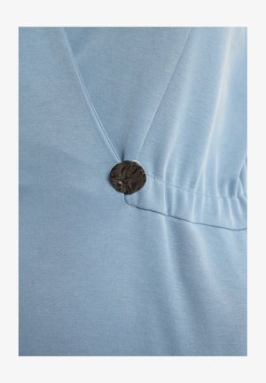 Jasnoniebieska tkanina o gładkiej fakturze, z ciemnym, teksturowanym guzikiem akcentującym marszczenie.