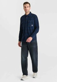 Blauw geruit flanellen overhemd met twee borstzakken, gecombineerd met donkere denim jeans en lichtgekleurde sneakers. Casual, ontspannen pasvorm.