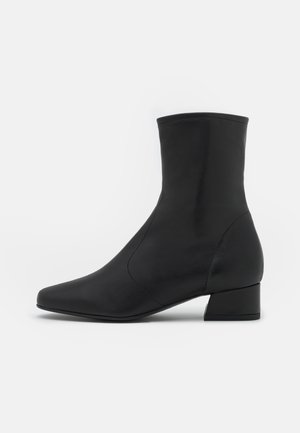 Botte en cuir noir mi-mollet avec petit talon bloc et bout pointu, présentée de profil sur un fond clair uni.