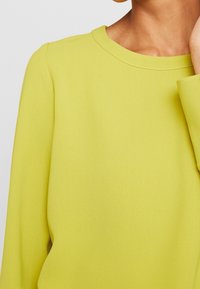 Pitkähihainen, pyöreäkauluksinen paita kirkkaan keltaisena, valmistettu pehmeästä, sileästä kankaasta, jossa on rento istuvuus ja minimaalinen sauman yksityiskohta.